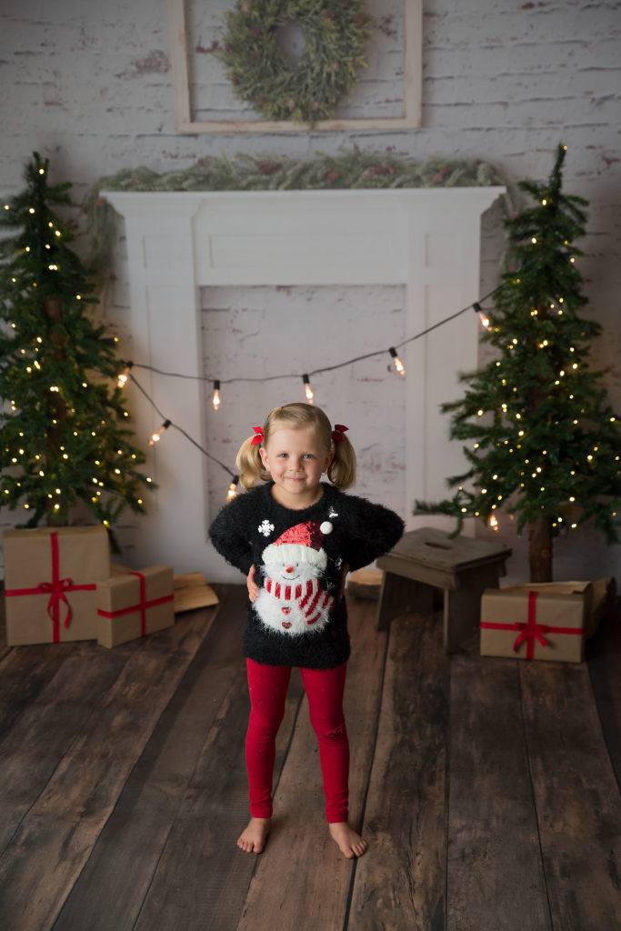 A cute blonde girl wears a snowman sweater during a Christmas mini photography session in Edmonton.