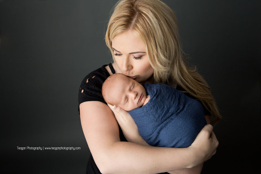 A new mother with blond hair hugs her newborn baby boy during an Edmonton photography shoot
