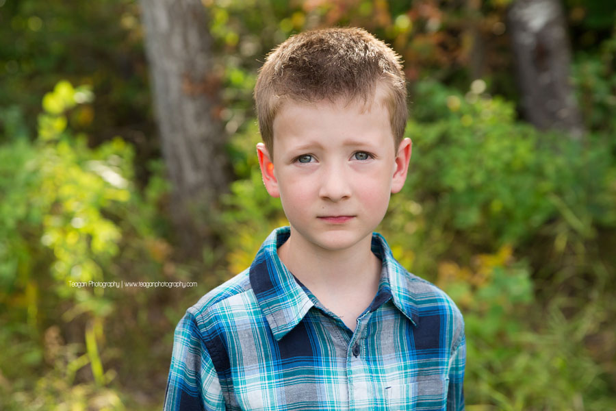 A school aged boy wearing a blue and black checkered button up shirt poses for a portrait in Edmonton