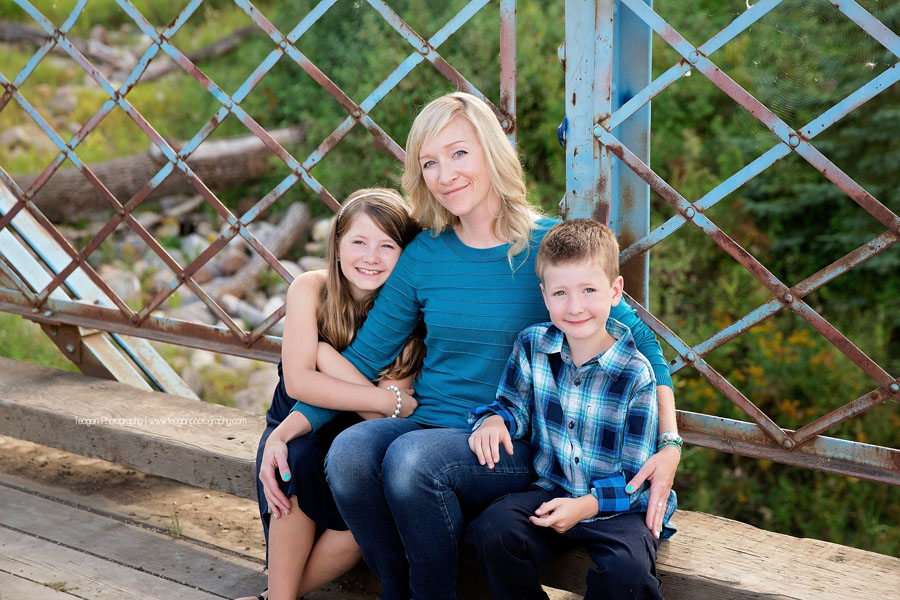 A mother hugs her two school age children during an Edmonton family photography session on a metal blue bridge