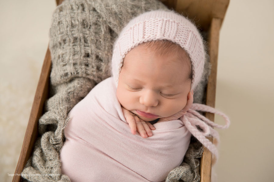 A baby girl is wrapped in pale pink and asleep in a wooden bed