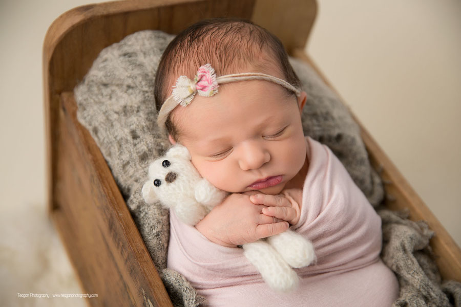 A baby girl is wrapped in pale pink and asleep in a wooden bed