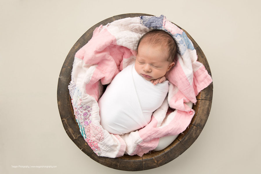 wrapped in white is a sleeping newborn baby girl with her hands tucked underneath her cheek
