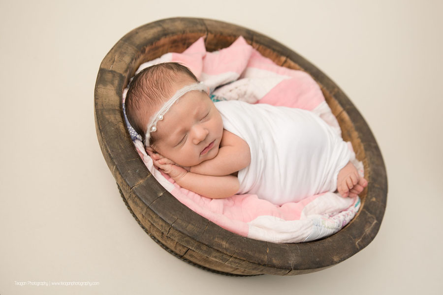 wrapped in white is a sleeping newborn baby girl with her hands tucked underneath her cheek