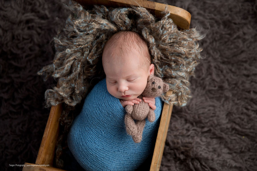 Wrapped in a blue scarf is a newborn baby boy asleep in a wooden bed