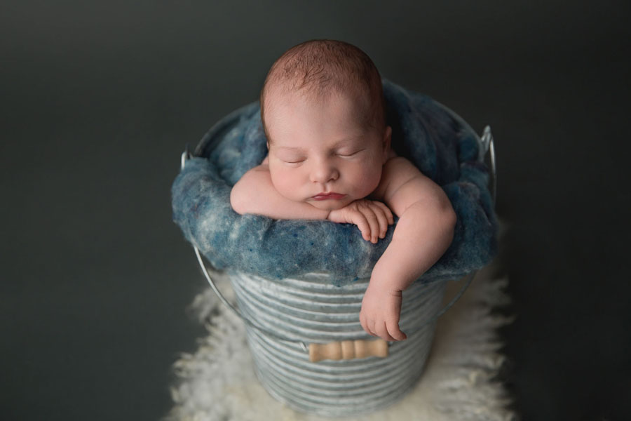 An Edmonton newborn baby sleeps in a metal bucket stuffed with denim blue wool fluff