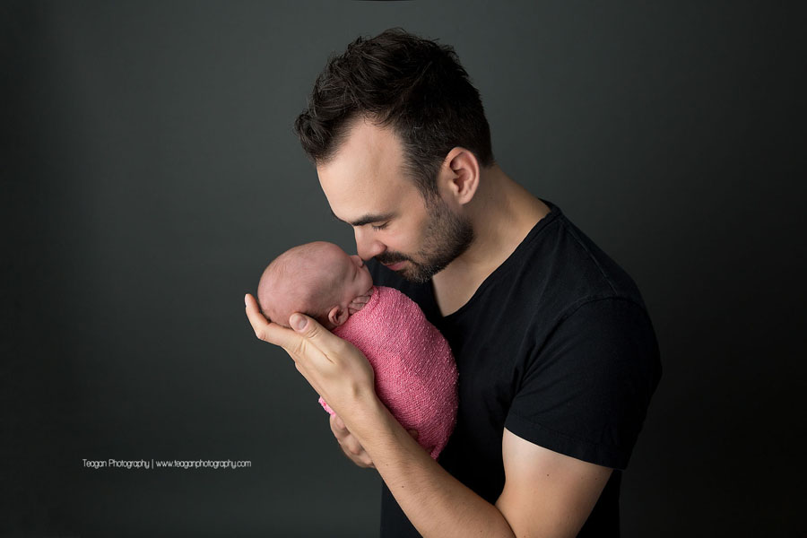 A new father cuddles his brand new baby girl who is wrapped in a pink blanket