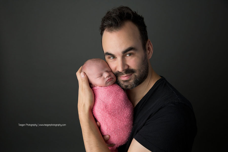 A new father cuddles his newborn girl who is wrapped in a pink blanket
