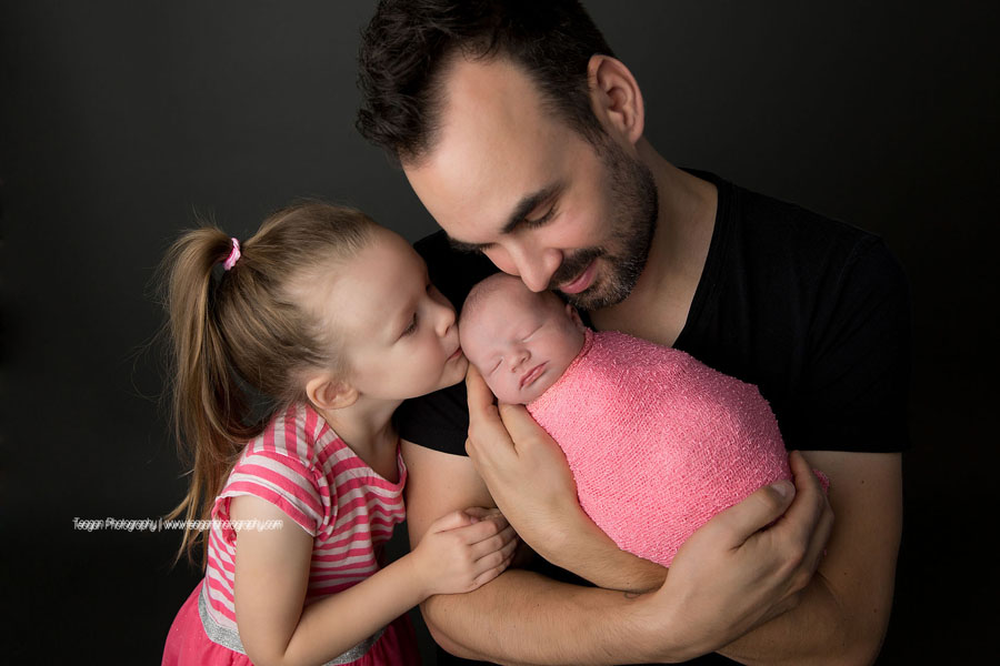 A father cuddles with his two daughters during an Edmonton newborn photography session