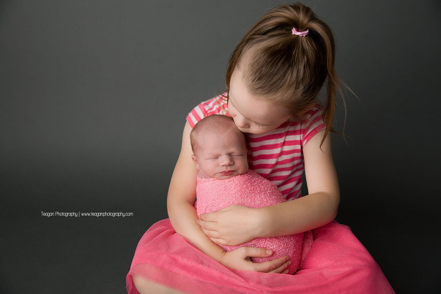 a big sister wearing matching pink clothes holds her newborn sister