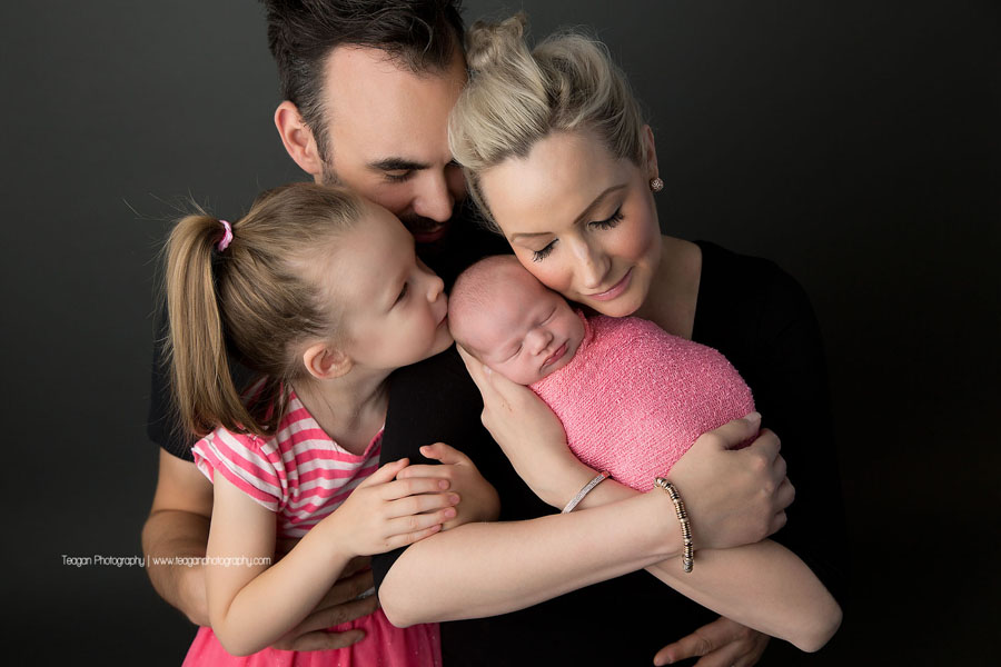 A family wearing pink and black pose together iwith their newborn baby girl during an Edmonton newborn photography session.