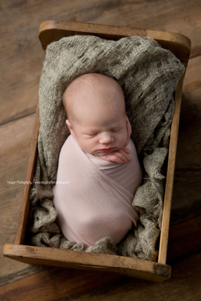 tucked in tight to a small wooden baby bed is a sleeping Edmonton newborn baby