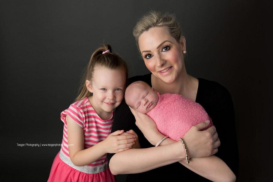 A mother cuddles with her two daughters during an Edmonton newborn photography session