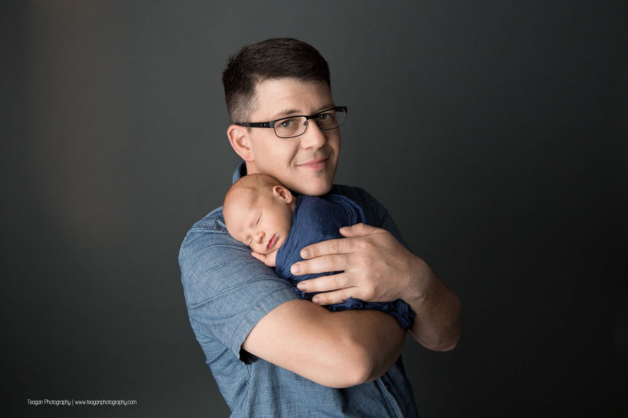 A new father snuggles his newborn baby boy during an Edmonton photography shoot