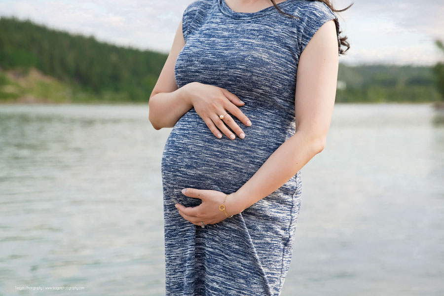 A Chinese woman hugs her tummy during a maternity session in the Edmonton river valley