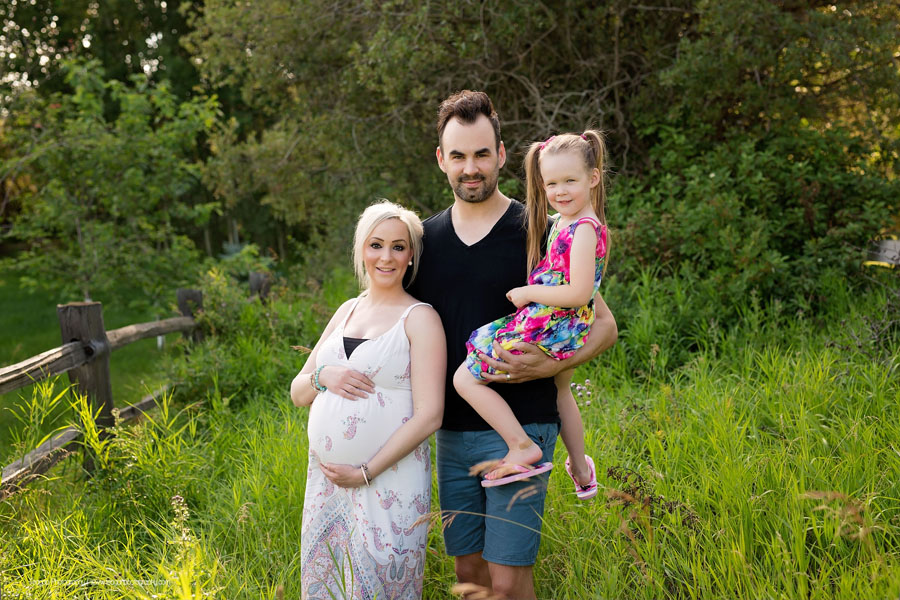 Mom and dad snuggle their toddler daughter in tall grasses during an maternity session