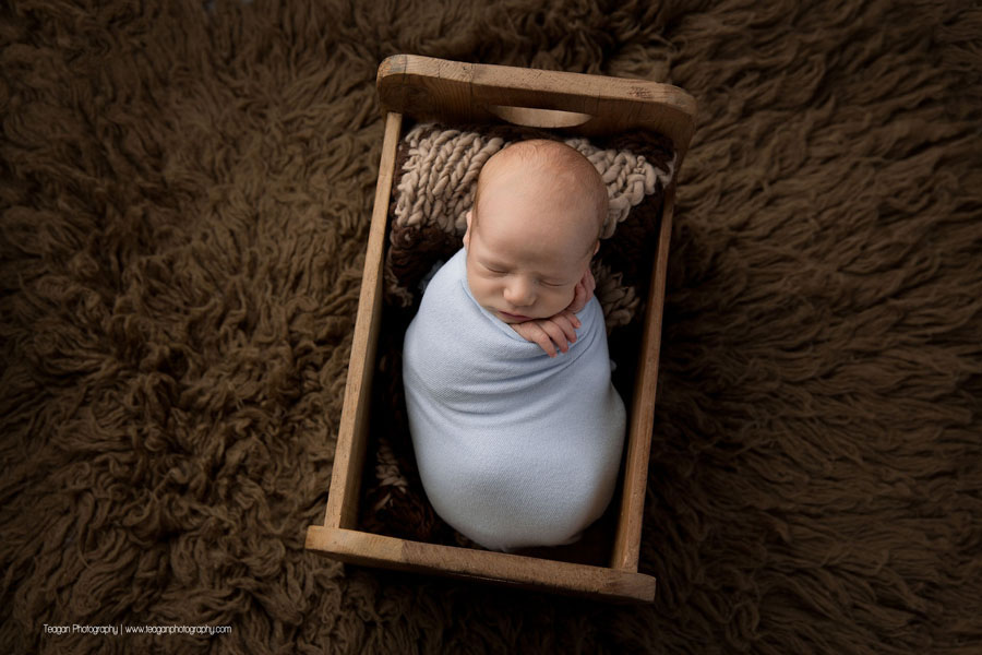 Sleeping in a small wooden bed is a newborn baby boy