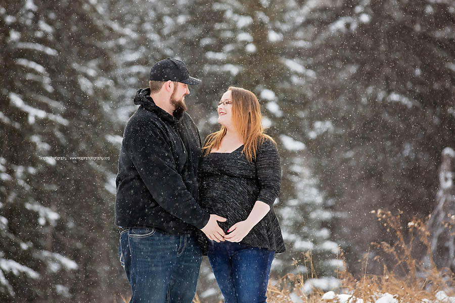 Couple posing in falling snow near Snow Valley Edmonton for outdoor maternity portrait