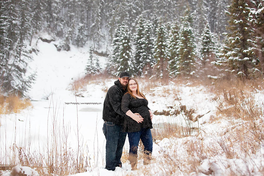 Couple posing in falling snow near Snow Valley Edmonton for outdoor maternity portrait