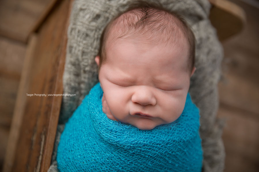 Wrapped in a turquiose blanket is a sleeping newborn baby boy