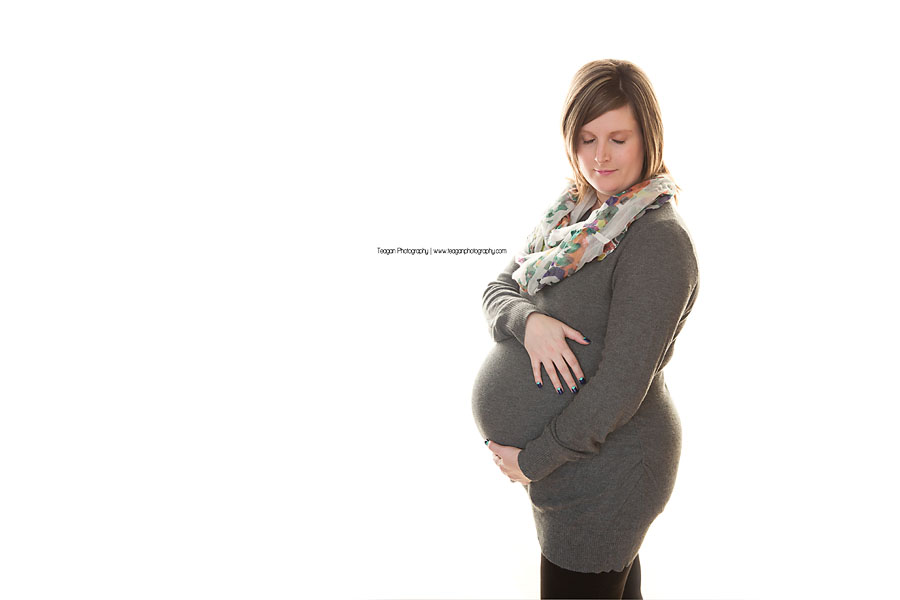 An Edmonton mother in a grey sweater hugs her pregnant belly during a maternity photoshoot