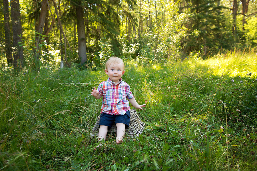 A ones year old boy sits on a basket in the grass at Larch Sanctuary in Edmonton