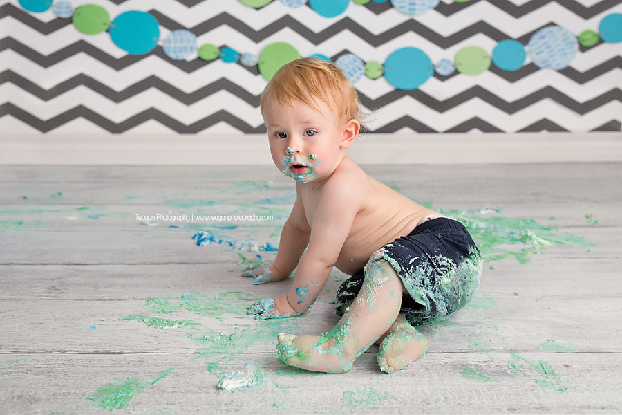 A blonde boy covered in icing crawls away during his Edmonton cake smash Photography session