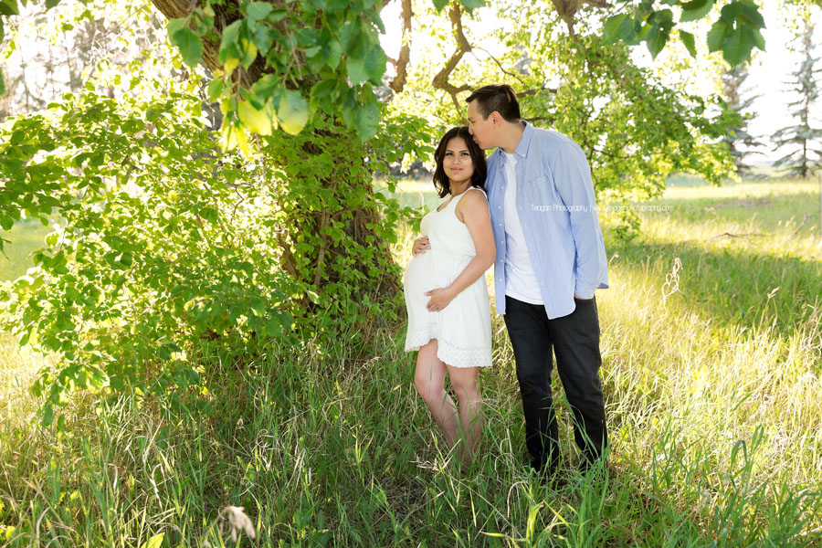 A beautiful pregnant woman hugs her belly while posing for maternity photos in an Edmonton field