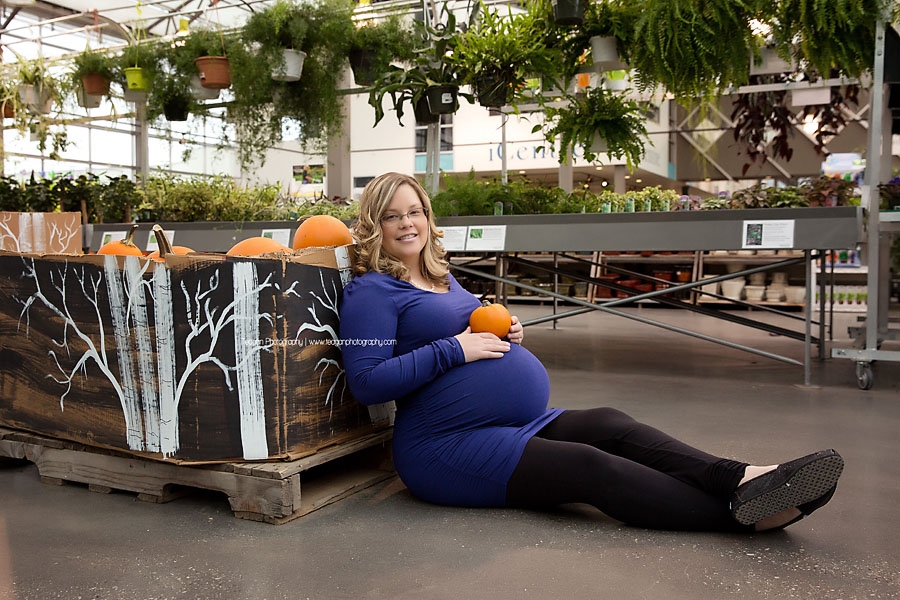 A mom in a blue maternity shirt holds a pumpkin next to her pregnant belly