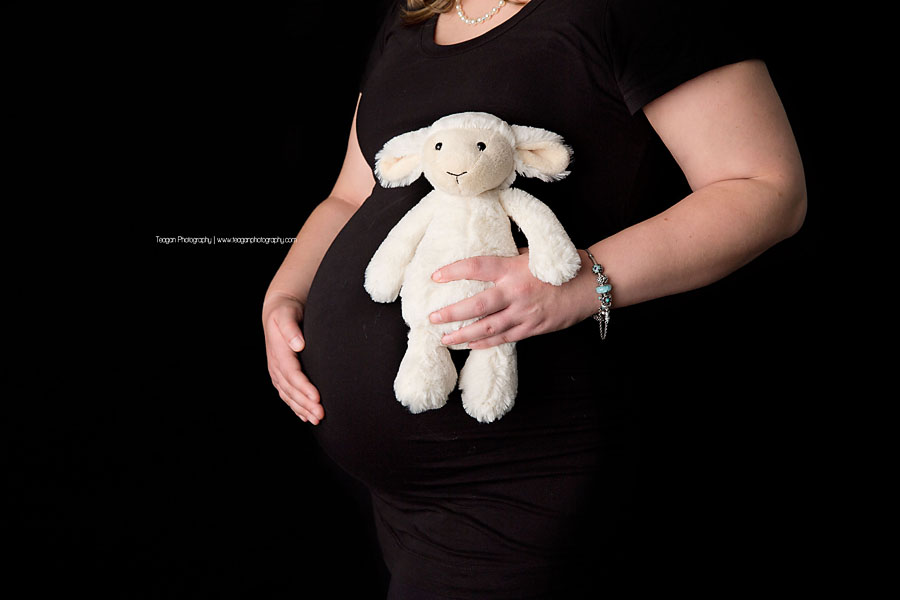 A woman holds a white toy lamb to up to her pregnant belly