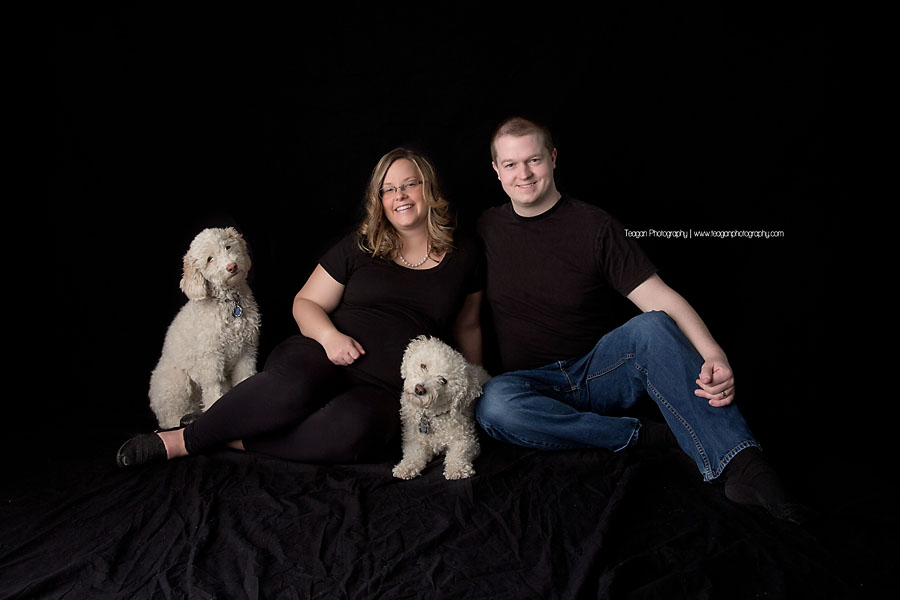 A couple sits on a black blanket with their two white dogs. 