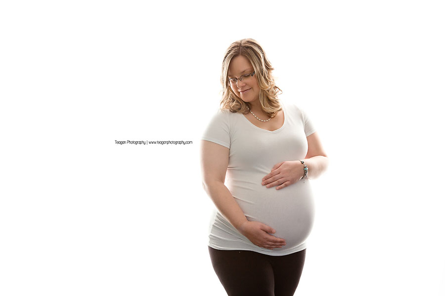 A beautiful mother to be hugs her belly in front of a glowing white wall