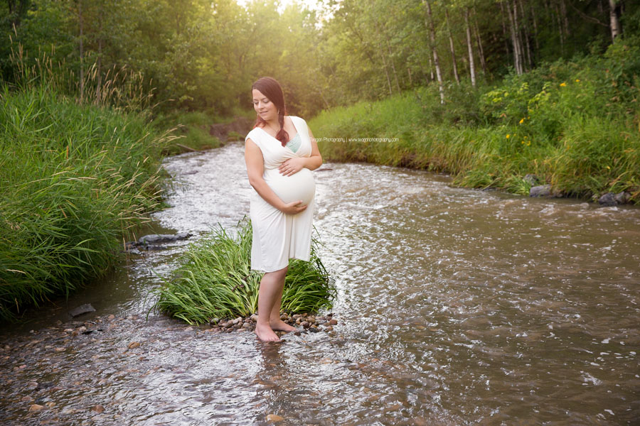 A pregnant Edmonton mother in a white dress poses during maternity photos in the Millcreek Ravine