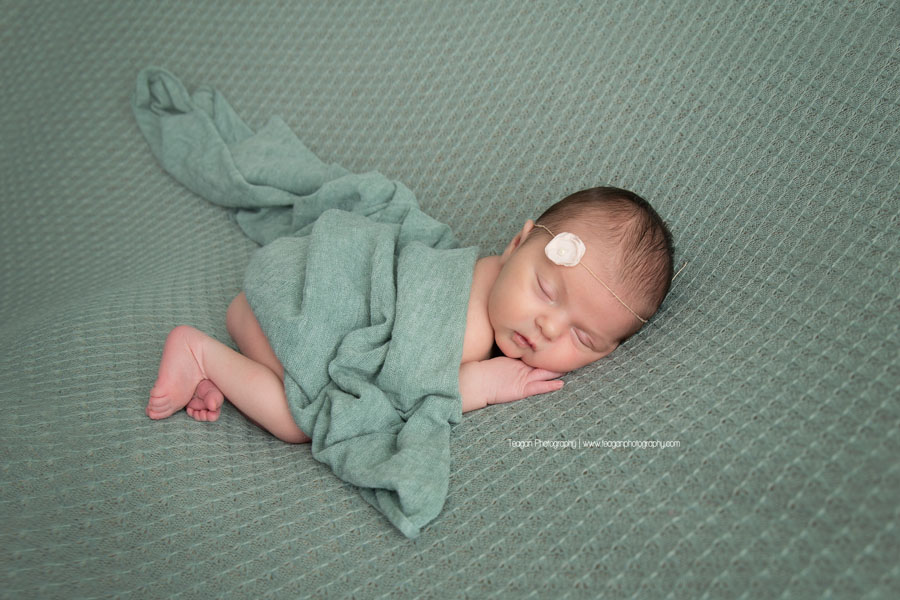 peeking out of a green blanket is a newborn baby girl