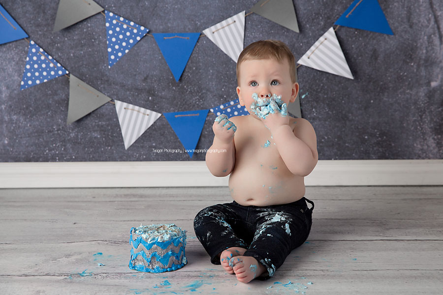 A one year old boy joyfully eats his blue iced cake during an Edmonton cake smash photography session