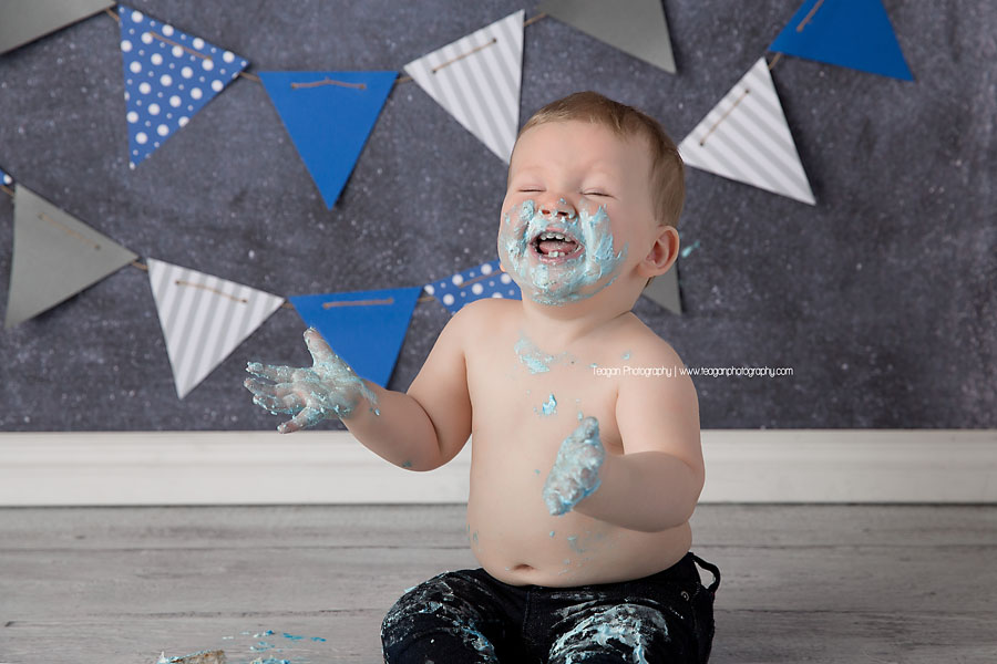 A one year old boy joyfully eats his blue iced cake during an Edmonton cake smash photography session