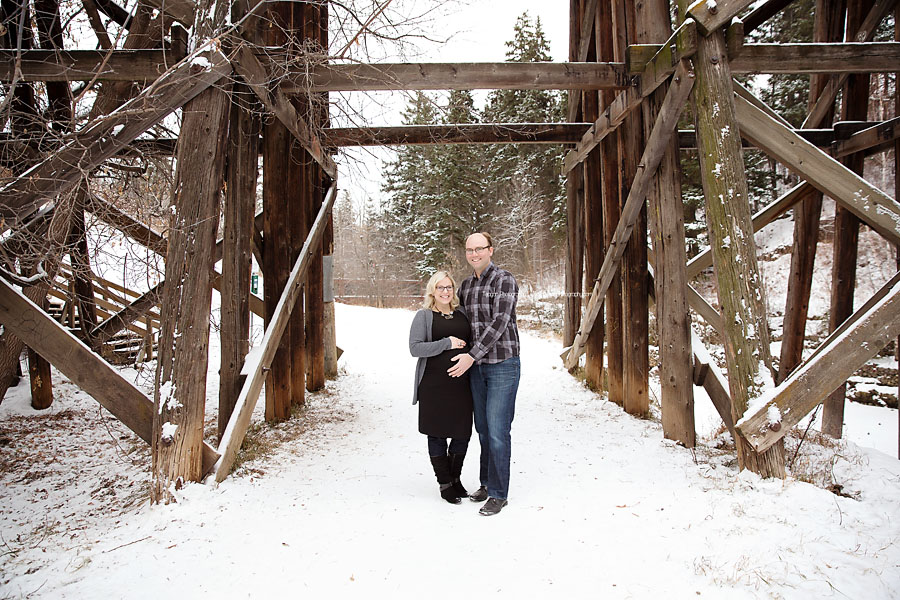 A pregnant couple stands belwo the Millcreek treselt bridge during a winter maternity photo shoot