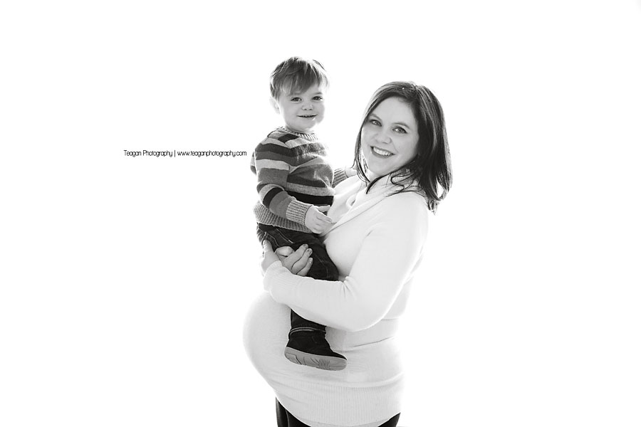 A burgundy haired mother wearing a white sweater poses for maternity photos at a top Edmonton studio