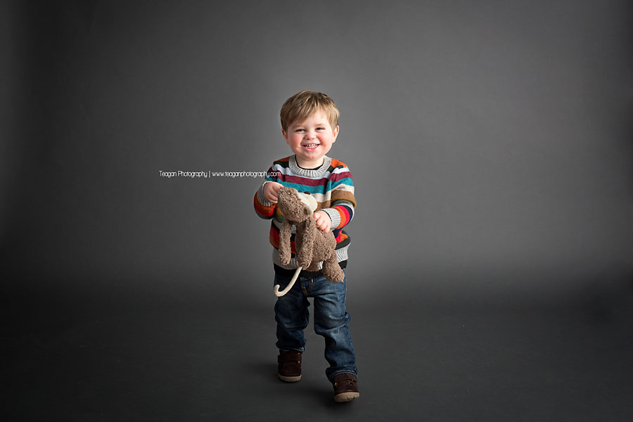 A cheeky little boy laughs as he stands on a grey backdrop