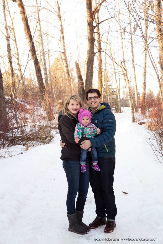 Parents snuggle with their one year old daughter in a forest in St Albert