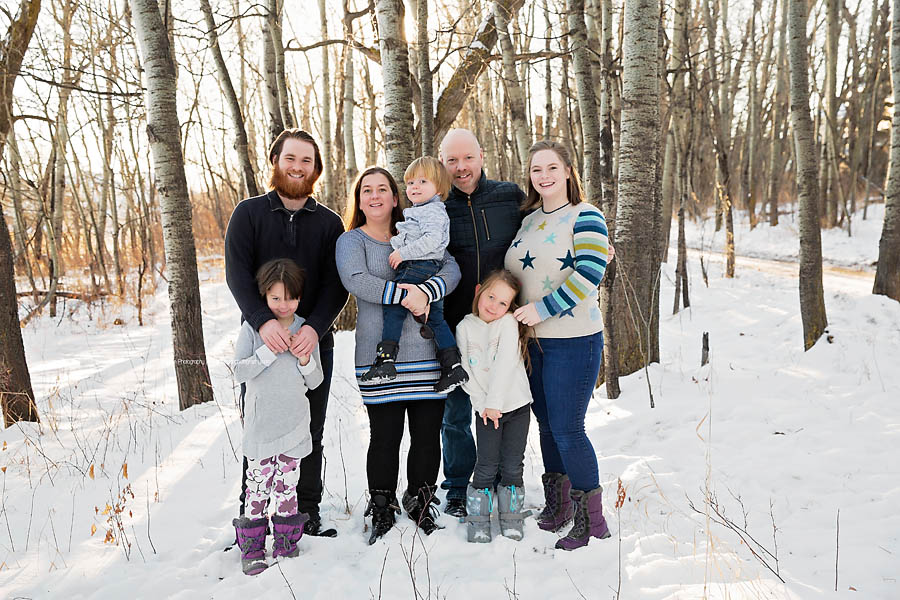 An extended family poses together in a sunlit poplar forest for winter photos in Edmonton. 