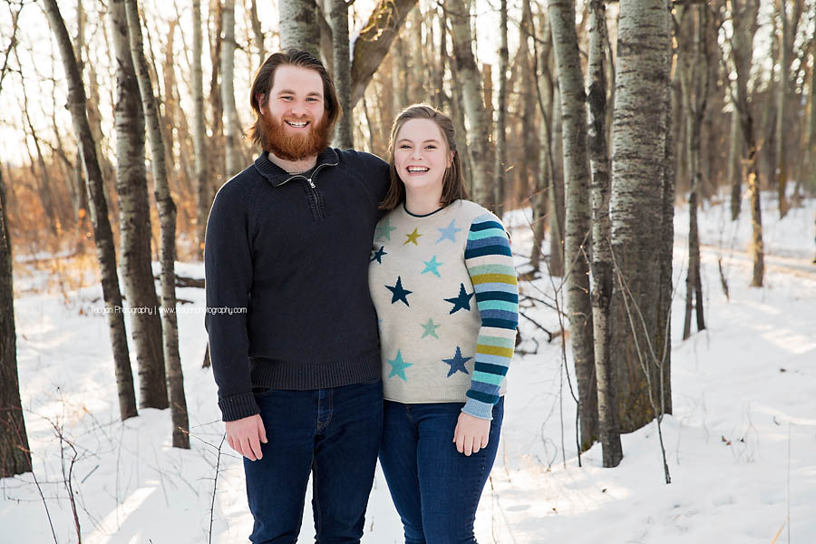 Adult siblings stand together in a winter forest during an Edmonton photo session
