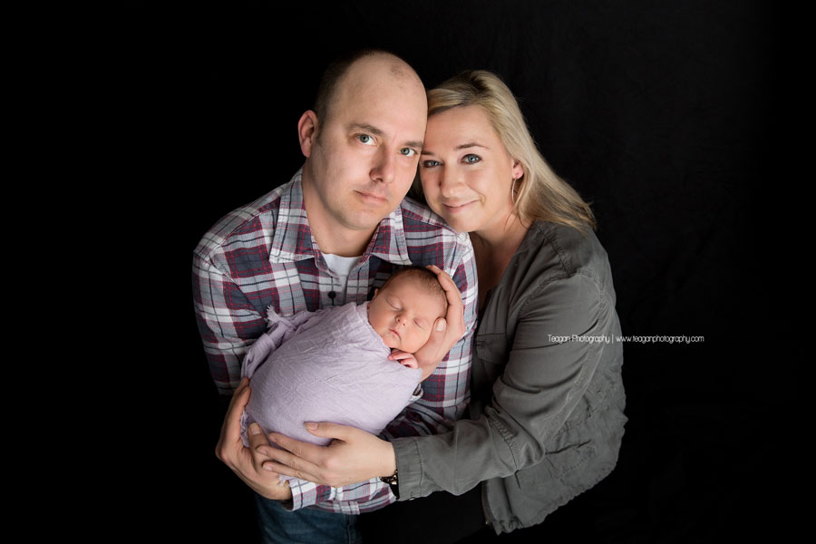 Mom and dad snuggle with their new baby while having photos taken  at an Edmonton Newborn photography studio