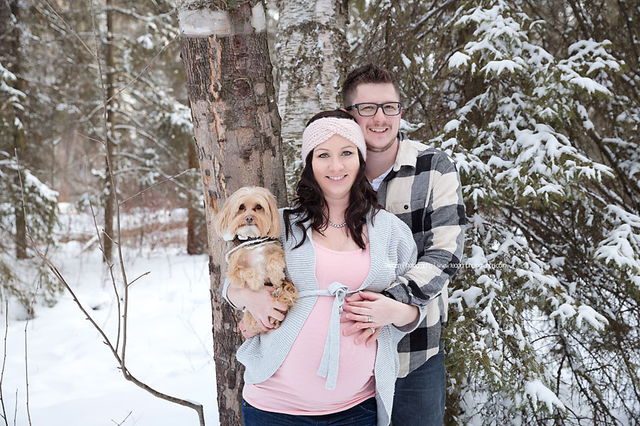 A pregnant couple poses with their terrier dog in the snow covered forests of Edmonton's River valley