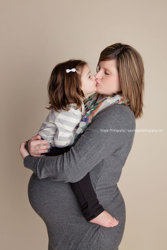 A toddler girl kisses her pregnant mother's tummy