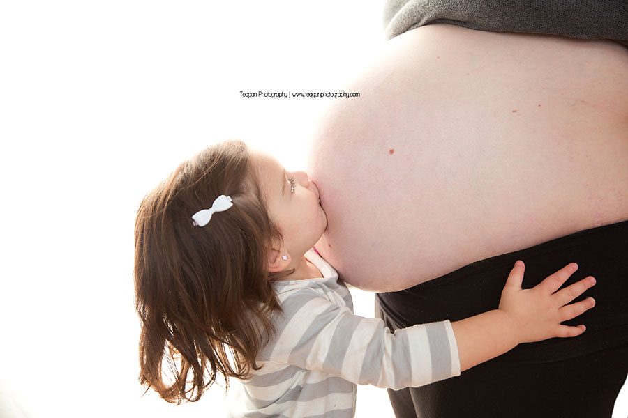 A toddler girl kisses her pregnant mother's tummy