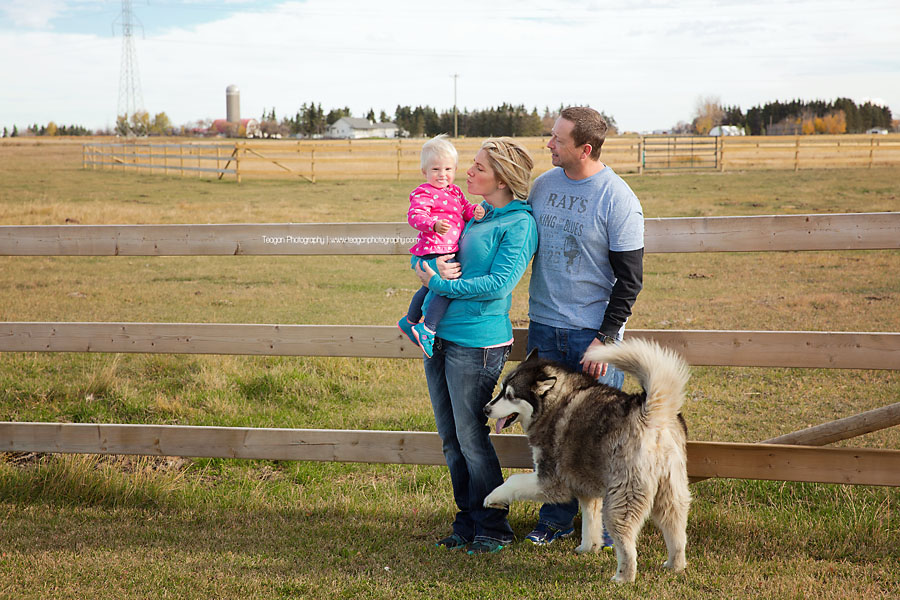 A family poses next to a wooden farm fence during Fall photos in Edmonton