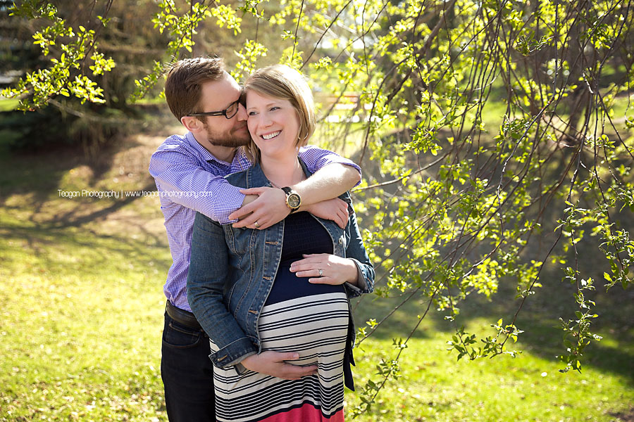 A father hugs his pregnant wife in the new leaves on a tree