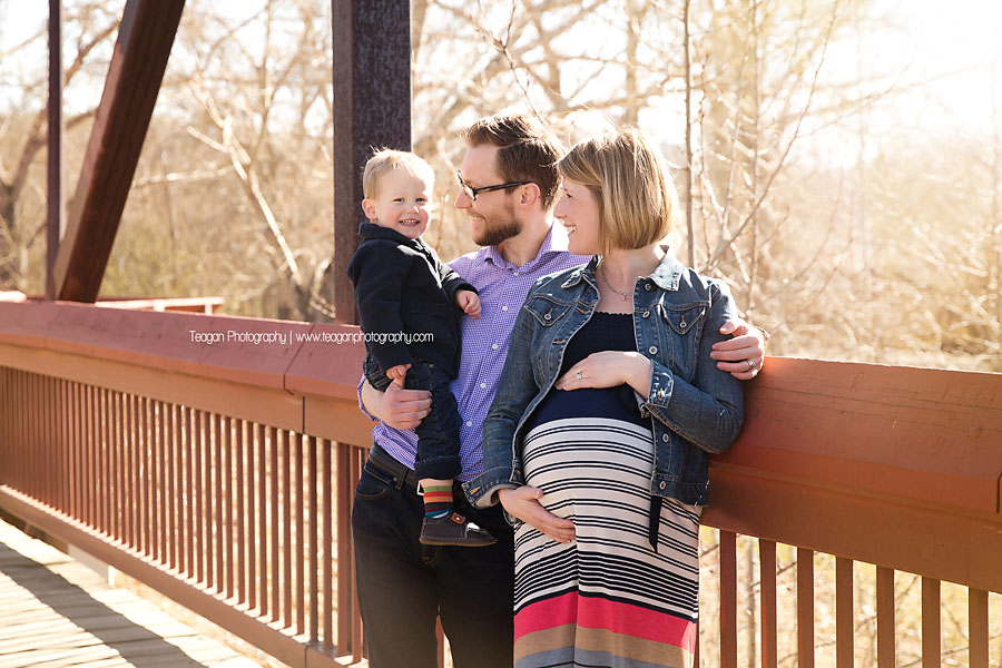 A family of three stands in the sunsine on an Edmonton footbridge