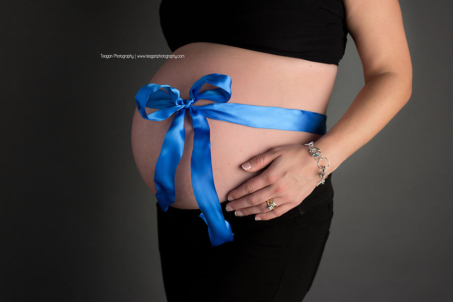 A blue ribbon is wrapped around the bare belly of a pregnant woman